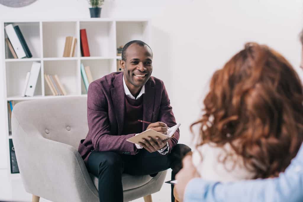 Smiling therapist talking to young woman in his office while taking notes